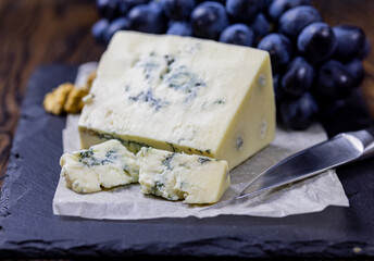 Tasty blue cheese served with grape and green on a wooden background. Dorblu cheese pieces