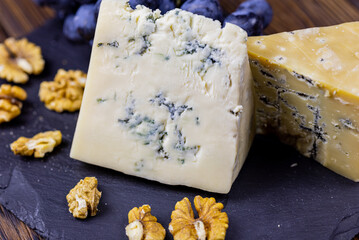 Tasty blue cheese served with grape and green on a wooden background. Dorblu cheese pieces