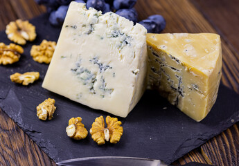 Tasty blue cheese served with grape and green on a wooden background. Dorblu cheese pieces