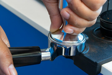 Barista hand tamping freshly ground coffee in stainless steel portafilter, preparing espresso for professional coffee machine in modern café setting. Perfect for illustrating barista skills