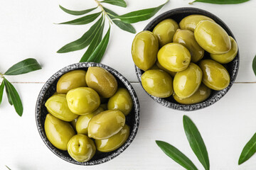 Composition with bowls of tasty green olives and leaves on light wooden background, closeup