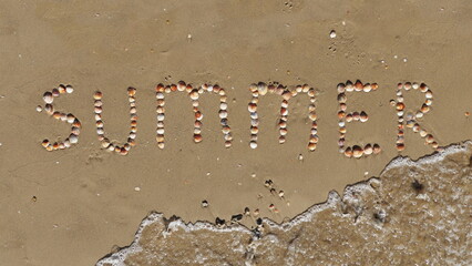 Summer inscription on the sand. The word summer laid out with shells on the sand and a sea wave. Letters made by Shells. Black and white Photo.