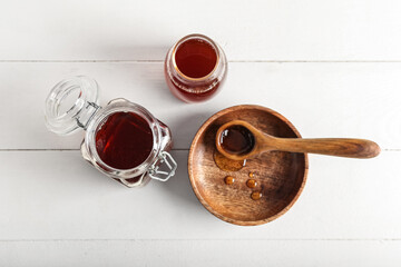 Jar, bottle and spoon with tasty maple syrup on light wooden background