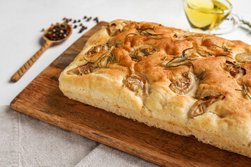 Wooden board with tasty Italian focaccia on light background, closeup