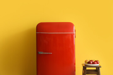 Plate with apples on stool and red fridge near yellow wall