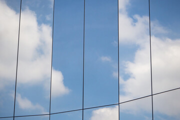 Reflection of clouds and blue sky on the surface of the glass wall of a modern building in a vertical frame