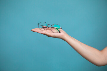 Female hand with stylish glasses on colorful background