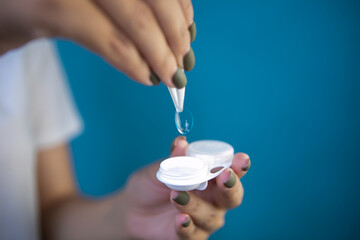Woman with contact lens and tweezers on blue background, closeup