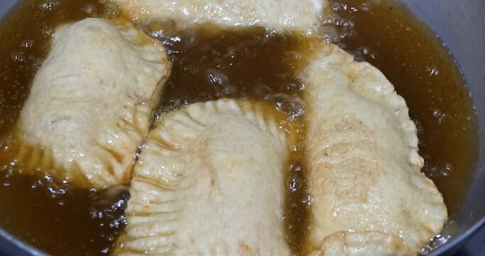 Frying Panzerotti. Female hands turn over apulian panzerotti patties, which are fried in olive oil in a large frying pan. Panzerotti is a traditional dish Puglia, Italia