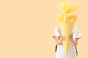 Cute little girl with yellow school cone on beige background