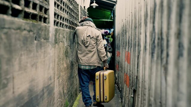 4K, Taken from behind a homeless Asian man carrying a bag in a narrow alley looking for work and food from people to donate. An elderly man with no work, no home, had to live on the roadside.