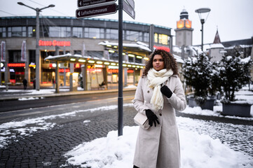 beautiful colored woman while shoping in a snow covered city wearing a white coat