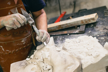 Man sculptor creates sculpt bust gypsum human woman sculpture with hammer. Statue craft creation workshop.