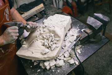 Man sculptor creates sculpt bust gypsum human woman sculpture with hammer. Statue craft creation workshop.