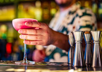 man hand bartender holding pink sweet and sour refreshing cocktail in glass on the bar counter
