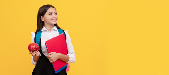 Happy kid smile holding books and apple yellow background, school snack. Horizontal isolated poster of school girl student. Banner header portrait of schoolgirl copy space.