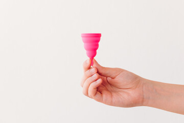A woman's hand showing a menstrual cup isolated on a neutral background. Zero waste, eco and...