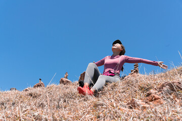 Fototapeta na wymiar Happiness Asian woman sitting on mountain with blue sky and open wide her arm to get natural fresh air.