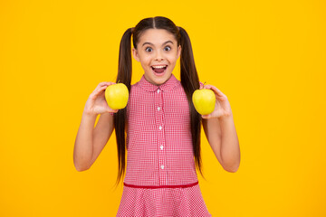 Child girl eating an apple over isolated yellow background. Tennager with fruit. Amazed teenager. Excited teen girl.