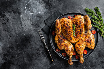 Tobacco whole chicken on plate with herbs and tomato. Black background. Top view. Copy space