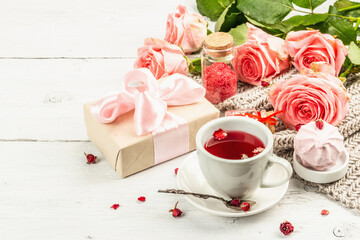 The concept of romantic tea. Wrapped gift, hibiscus tea, a bouquet of delicate roses, sweets