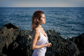 Fototapeta na wymiar Peaceful lady with ship miniature in hands standing on rocky seashore