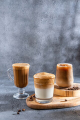 Ice coffee in a tall glass with cream poured over and coffee beans. Set with different types of coffee drinks on a dark table.