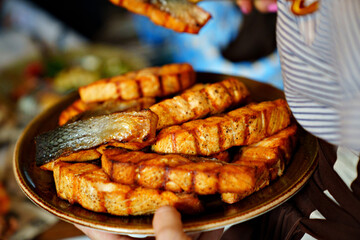 a plate of red fish fried on the grill in the hands of a waiter.