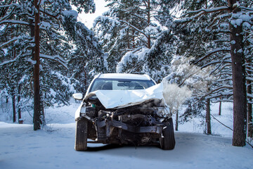 Front view of a crashed car wreck in winter forest snow after the accident with smoke coming out...