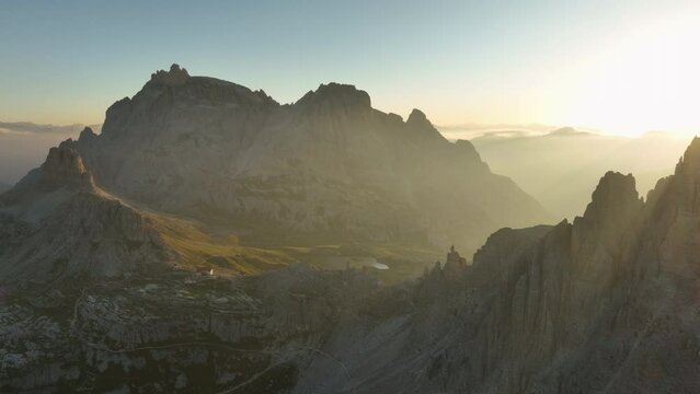 View from above, stunning aerial view of a mountain range during a beautiful sunrise with a mountain hut in the distance. Tre Cime di Lavaredo, Dolomites, Italy.