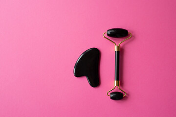 Black gua sha scraper and roller on pink background