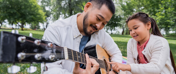 Smiling asian family playing acoustic guitar in park, banner.