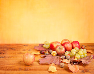 wooden table with apples, grapes and autumn leaves on a yellow background with copy space