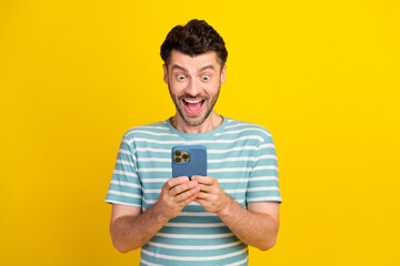 Photo of funny ecstatic handsome guy dressed striped t-shirt look on smartphone read message impressed sale on yellow color background