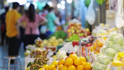 Assortment of fresh fruits at market. Blurred people are shopping in background. - Powered by Adobe