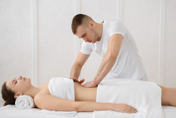 Close up of osteopath doing manipulative massage on woman abdomen on white background, copy space