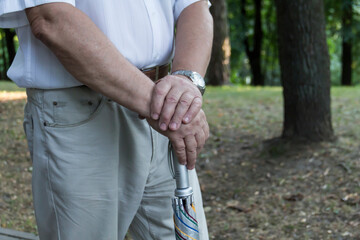 The large hands of an elderly man are folded on a cane with a watch on his right hand