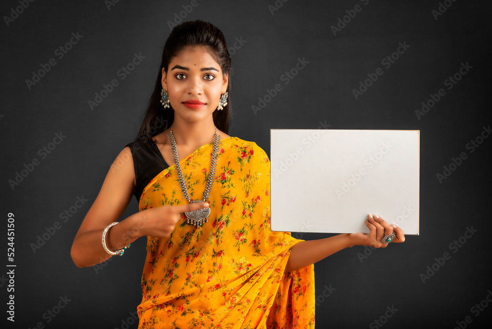 Wall mural A young girl or businesswoman wearing a saree and holding a signboard in her hands on a gray background.