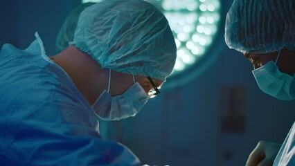 A close up shot of the male surgeon wearing glasses and concentrating on his surgery while being in a dimly lit hospital room - Powered by Adobe