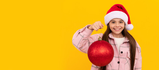 Fototapeta na wymiar happy teen girl in santa claus hat hold christmas decorative ball on yellow background, new year. Banner of christmas child girl, studio kid winter portrait with copy space.