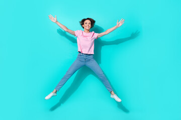 Fototapeta na wymiar Full size photo of nice cute woman wear pink t-shirt jeans white sneakers jumping high having fun isolated on turquoise color background