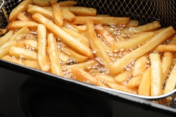 Cooking delicious french fries in hot oil, closeup