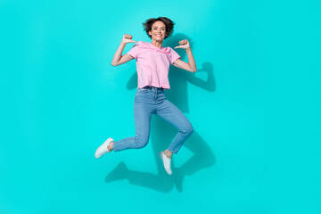 Full length photo of lovely girl pink t-shirt jeans white sneakers directing herself flying jumping isolated on turquoise color background