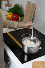 Woman cooking dumplings in saucepan with boiling water on cooktop, closeup