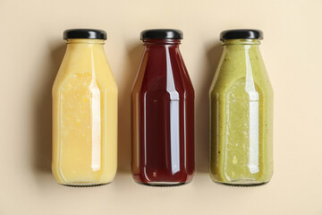 Bottles with delicious colorful juices on beige background, flat lay