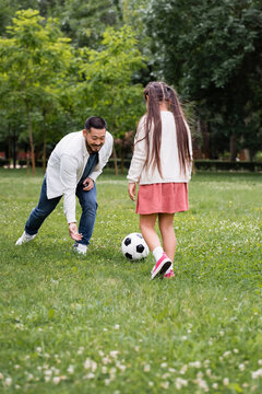 Happy asian father playing soccer with daughter on grass in park.