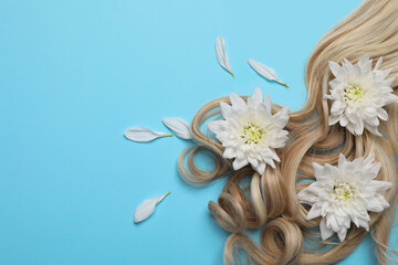 Lock of healthy blond hair with flowers on light blue background, flat lay. Space for text