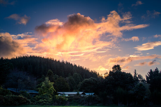 Beautiful HDR scene of late sunset with flaming sky over darken ground and silhouettes of foresty hills. Small farmhouse nested at the bottom of hill. Taupo, New Zealand