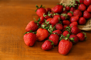 Basket with scattered ripe strawberries on wooden table, closeup