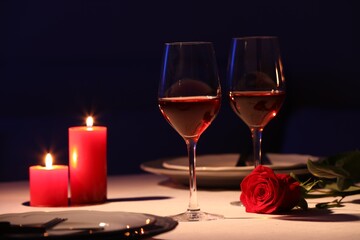 Beautiful table setting with glasses of wine, candles and rose in dark room. Romantic dinner for Valentine's day
